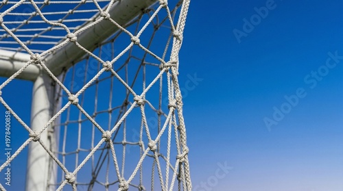 Close-up of a white soccer goal net against a clear blue sky background. Concept of goal achievement, sports championship, match day, and competition victory at the stadium. Copy space.
