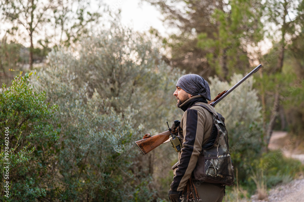 Fototapeta premium Hunter walking forest path carrying shotgun