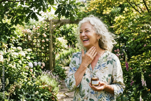 Radiant senior woman with white hair laughing in lush summer garden while holding organic face cream jar