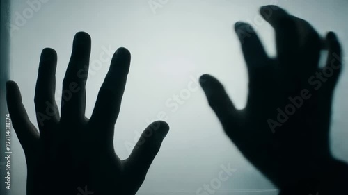 Silhouetted hands touching a frosted glass surface in a dark and mysterious foggy environment