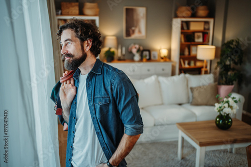 Bearded man contemplating future looking out window home