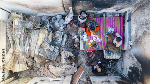 Aerial view of a family sitting on a mat amidst the charred remains of their home, a stark contrast of life and devastation, Dhaka, Dhaka Division, Bangladesh.