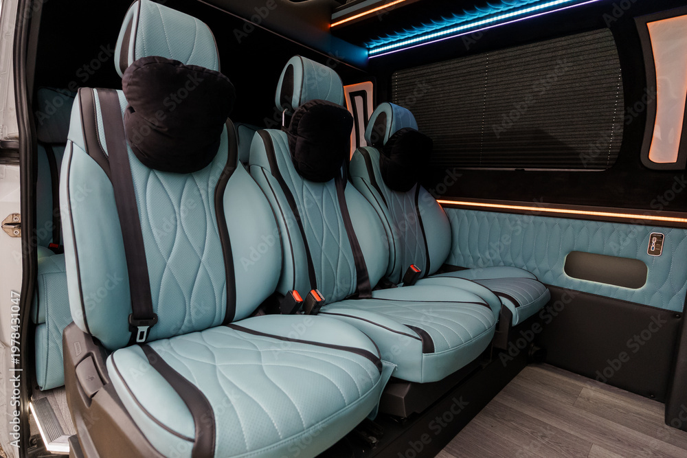 Obraz premium Interior of a luxury passenger van featuring light blue quilted leather seats and ambient blue LED lighting.