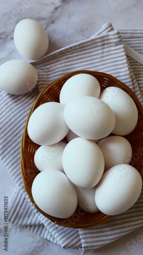 A woven basket brimming with white eggs sits on a striped linen, highlighting the beauty of simplicity and freshness in a warm kitchen.
