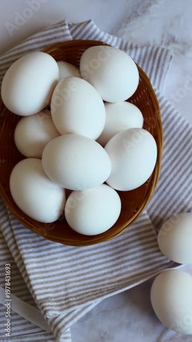 Fresh white eggs in a woven basket on a striped cloth, perfect for breakfast or baking treats