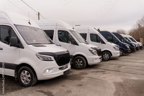 Fotografie Row of white and dark delivery vans parked on asphalt lot under overcast sky in outdoor setting