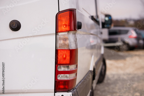 Close up of red and white rear taillight on white commercial delivery van parked outdoors in daylight.