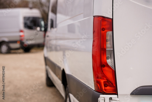 Close up of a white commercial transport van with red tail light parked in an outdoor setting.