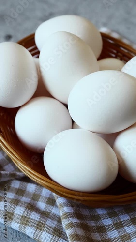 A rustic woven basket holds a collection of fresh white eggs resting on a charming checkered cloth, creating a cozy kitchen atmosphere.