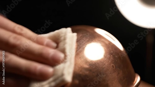 Close up of a hand polishing a copper bowl with a white cloth against a dark background for cleaning and restoration concept and meticulous care