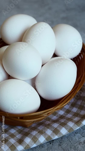 Fresh white eggs in a rustic basket on a checkered cloth, symbolizing simplicity and home cooking