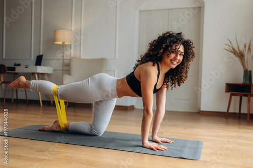Canvastavla Young woman with curly hair performs leg exercise using resistance band on yoga