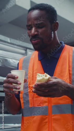 Blue collar worker in the metal processing industry, having a lunch break, eating his sandwich outdoors near a manufacturing facility.