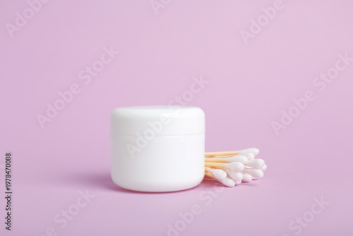 White plastic jar and cotton swabs on a pink background
