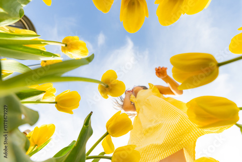 Little girl in yellow dress among tulips low angle view