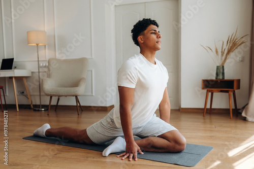 Billede på lærred Young male practicing yoga in a modern indoor setting, performing a pigeon pose