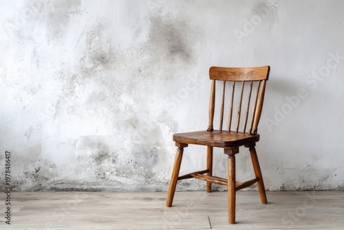Wooden chair stands against a distressed textured wall with light wood floor.