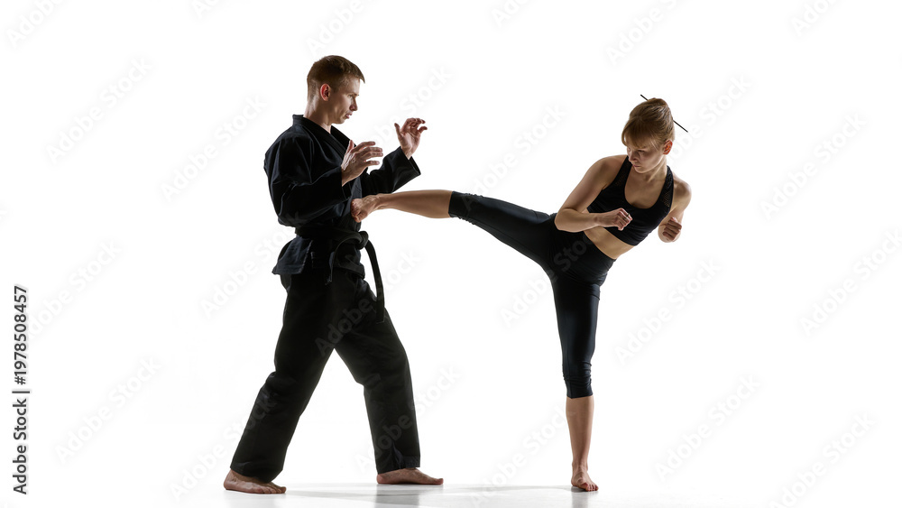 Obraz premium Woman delivering high side kick during martial arts training with partner. Concept of fitness training program, combat sport class, strength conditioning and flexibility improvement.