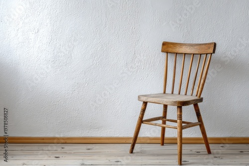 Wooden chair sits against a textured white wall on a floor.