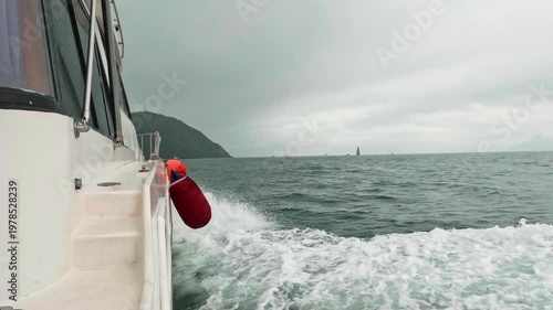 A motorboat fast sails across the sea during cloudy, choppy weather, as seen from the side. Waves splash in all directions