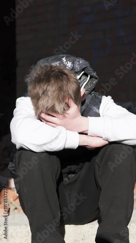 A lonely teenage boy sits in an abandoned brick building after school, away from people. The sunlight highlights his face as he reflects in solitude. The scene conveys themes of bullying, isolation.