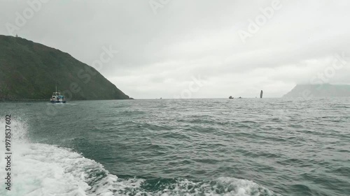 A view from a motorboat in the open Pacific Ocean during cloudy, choppy weather. Waves splash from below in all directions