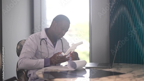 African American male doctor writing prescription on clipboard at desk, Orthopedic physician working with medical record, laptop and knee model in clinic, Healthcare and physical therapy concept