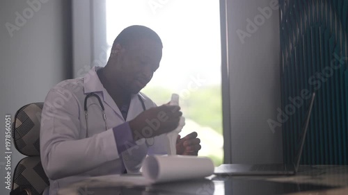 African American male physical therapist doctor looking at laptop holding anatomical knee joint model in rehabilitation center, Orthopedic medical clinic, healthcare and physiotherapy concept