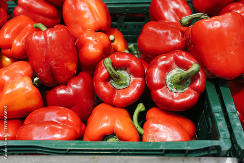 Red bell peppers in crate at market. Fresh vegetables display. Organic produce for cooking. Healthy food ingredient with vibrant color and natural texture close up.