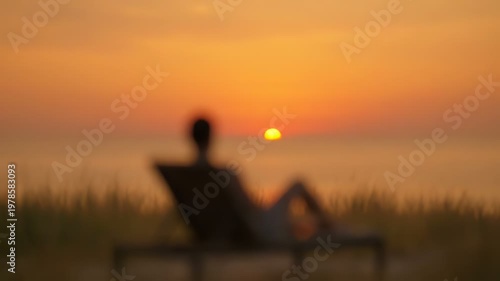 Man relaxing on lounge chair at sunset, watching the sun over the ocean horizon.