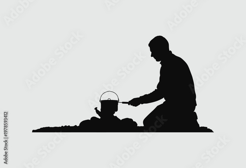 A silhouette of a man kneeling on the ground while cooking food over an open campfire outdoors