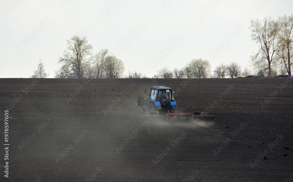 Fototapeta premium Tractor working in a dusty field, preparing soil for planting