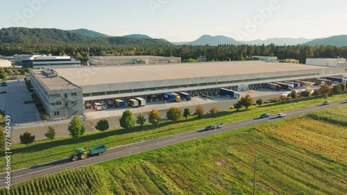 Large logistics center shows trucks loading and unloading cargo in the distribution area with mountains in the background and clear skies.