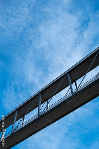 Diagonal skybridge walkway in steel glass and sky presented as abstract architecture with modern minimal structure and restrained geometry