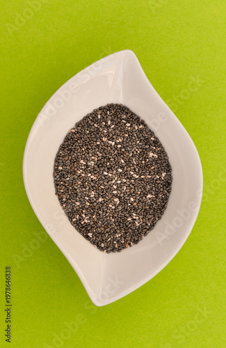 Chia seeds in white leaf shaped bowl on green background, overhead view