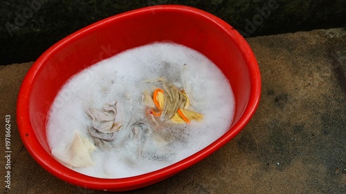 Quadro su tela close up of a red plastic basin filled with soapy water and submerged fabrics fo
