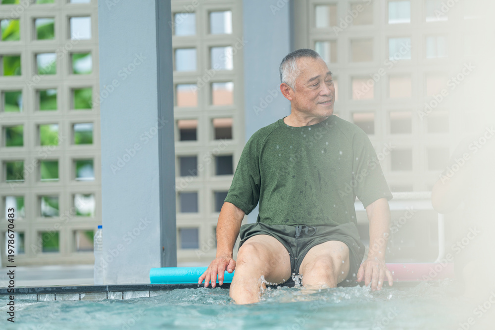 Fototapeta premium Smiling older man enjoying aqua therapy at the pool edge. Active senior in wet clothes kicking water for physical rehabilitation and fitness. Healthy aging and outdoor leisure activity.