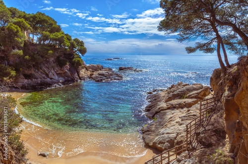 Картината върху платно Panoramic view from the top of a secluded cove with crystal clear turquoise waters and rocky cliffs, and the Camí de Ronda winding protected by wooden fences along the Costa Brava in Platja d'Aro