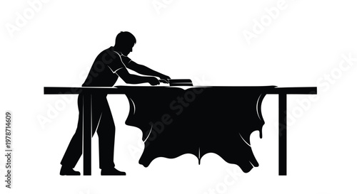 Silhouette of a man working on a large piece of leather on a table