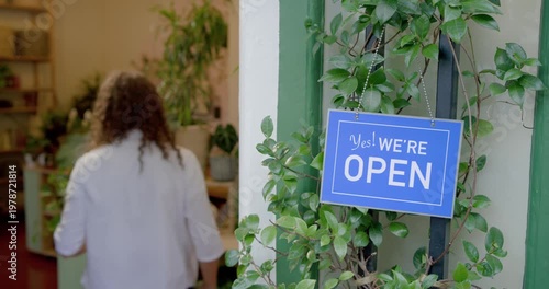 Non-binary owner flipping closed sign to open, entering shop, arranging potted plants, opening shop