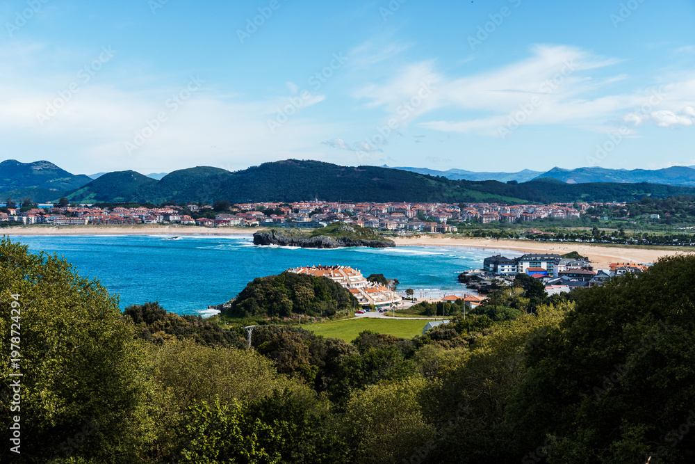 Fototapeta premium Scenic coastal view of Isla, Cantabria, featuring a town, beach, and sea under a blue sky.