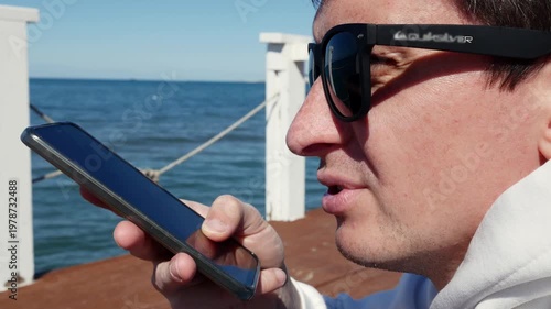 Man using smartphone voice assistant at the beach, mobile technology.