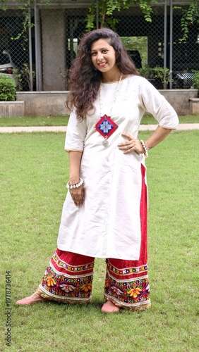 Indian woman in casual ethnic kurta with colorful embroidered palazzo pants, posing outdoors on grass, showcasing modern fusion fashion with traditional touch.