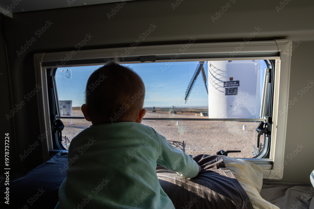 Obraz premium Baby looking out camper van window seeing windmill