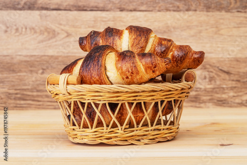 Freshly baked croissants in wicker basket close up on wooden background