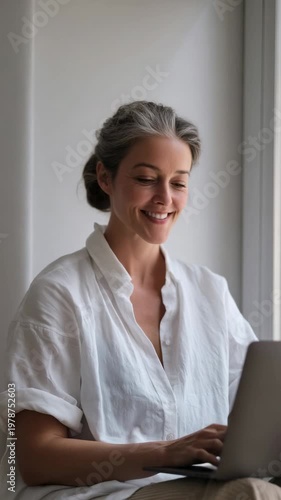 Woman working on laptop at home during daytime with sunlight shining through the window