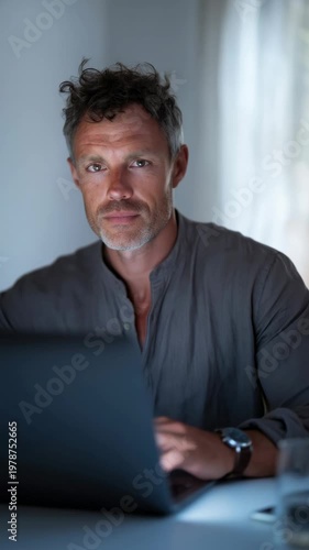 Focused man works on laptop at home in natural light during afternoon hours