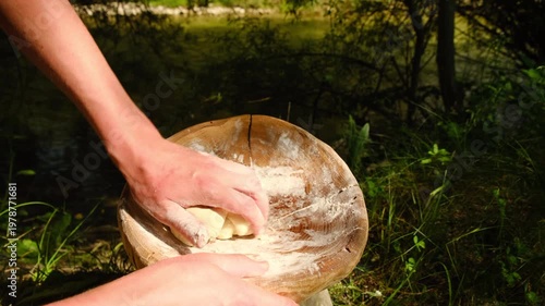 Male hands kneading dough in flour at outdoors. Baker kneads dough and making bread. Chef prepares dough with flour to make pasta. Baker hands close up. Preparing bread during camping