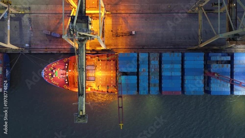 Container crane loading cargo ship at a busy port terminal at night with illuminated industrial activity