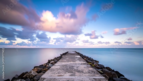 Concrete pier extending into tranquil ocean under a cloudy sky.